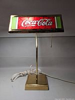Full view of Coca-Cola lamp showing brass metal base and stained glass style shade with logo.
