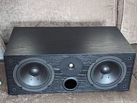 Front view showing two midrange drivers, one tweeter, and a central port of the black wood grain speaker cabinet.