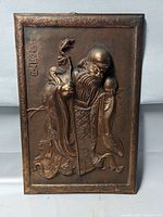 Front angled view of the embossed copper plaque showing figure, script, and texture detail.