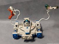 White and blue Fisher Price Adventure People Alpha Interceptor space ship with 3 astronaut figures attached by cords, front view showing cockpit and figures.