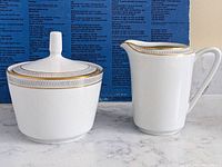 Photo of ceramic sugar bowl with lid and milk jug, showing gold and blue decorative rim bands.