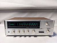 Front view of receiver showing silver faceplate, tuning dial and control knobs, wood veneer top visible.