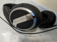 Close up of right ear cup showing Sennheiser logo, metallic and mesh design on ear cup, and cable attached.