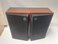 Front view of the pair of Tannoy speakers with wooden finish and black fabric grille covers showing slight wear.