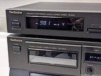 Close-up photo showing the front panels of the Technics Quartz Synthesizer AM/FM Stereo Tuner ST-K50 on top and the Stereo Double Cassette Deck RS-TR210 below, both with power buttons, displays, and control buttons visible.