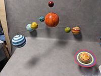 Full view of the planets mobile sculpture with planets arranged and suspended from metal rods showing the Sun, Earth, Saturn with rings, and other planets in varied colors.
