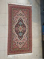 Top-down view of vintage rectangular rug with fringed edges, floral central medallion pattern and geometric borders on tiled floor