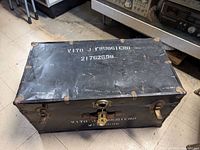 Full view of the closed soldier's trunk showing metal reinforcements and a lock with the name VITO J FRUGGIERO stenciled on top.