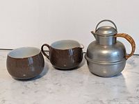 Full view of Denby milk jug, sugar bowl, and British pewter teapot with woven handle, showing front profile.