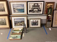Photo showing multiple framed prints and artworks arranged on floor including beach scenes, Eiffel Tower poster, floral print, box canvas paintings and metal Eiffel Tower sculpture.