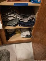 Photo of folded assorted bath and hand towels in multiple colors stacked on shelves inside a wooden cabinet.