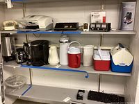 Shelves of vintage coffee makers, insulated carafes, coolers, and dispensers arranged against a wall, showing entire lot