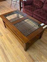 View of the coffee table illustrating the two-panel decorative glass top and wooden frame in living room.