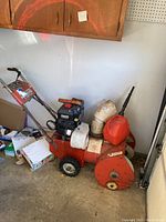 Orange and black craftsman snow blower with Briggs and Stratton motor viewed from side, showing gas cans on top, set in garage.