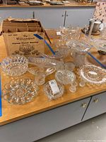 Wide view of multiple crystal ware items on table showing variety of platters, bowls, and cups including boxed punch service set.