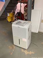 Full side and front view of white Danby dehumidifier on basement floor near mop bucket and utility shelves, showing size and condition.