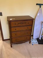 Front view of solid wood dresser showing floral design on top drawer and four drawers with wooden knobs.
