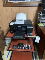 Epson ET-2720 printer with paper loaded and multiple ink cartridges displayed in front.