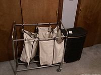 Metal laundry cart with three beige fabric hanging divider baskets and vintage vinyl-covered laundry basket to the side.