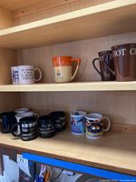 Shelf holding 10 assorted coffee mugs with varied designs and texts.