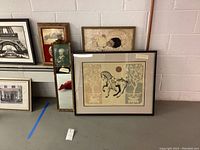 Wide view showing several framed art pieces, a wall mirror, and clock leaning against a wall.