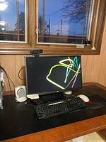 View of HP 24-inch monitor with webcam, Dell keyboard, Microsoft mouse on black mousepad, white speakers on a wooden desk by window.