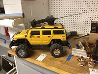 Side view of yellow remote control Hummer vehicle on a wooden surface next to other miscellaneous items with handheld remote control on top of vehicle.