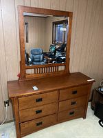 Full view of dresser with attached mirror showing six drawers and wood finish in a room with wood panel walls.
