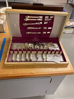 Wide photo of the 1847 Rogers Bros silver plated silverware set including knives, forks, and spoons in a wooden case with purple velvet lining.