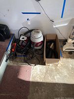Wide shot of Shop Vac, vacuum hose attachments in box, power drill, and other vacuum accessories on garage floor.