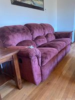 Full view of plum fabric sofa recliner next to wooden side table on wood floor
