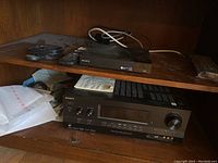 Sony Blu-ray player and A/V control center with speakers shown on wooden shelf. Remote control and cables visible.