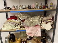 Shelving unit with assorted folded table linens including tablecloths, napkins, placemats and the brass napkin rings on a lower shelf
