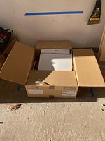 Washlet seat in open cardboard box, view from front