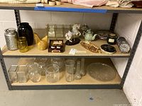 Wide view of metal shelving with assorted glass vases, teapots, figurines, and decorative plates arranged on shelves.