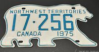 Front view of the 1975 Northwest Territories license plate shaped like a polar bear, showing the full plate with blue raised text and numbers on a white background.