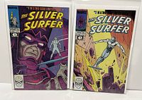 Photo shows front covers of The Silver Surfer comic books #1 and #2 sealed in plastic bags with backing boards, displaying both covers fully.