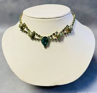 Front view of vintage 15” choker necklace with green rhinestones and beaded accents on white bust display.