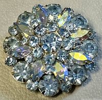 Close-up front view showing faceted blue round and iridescent marquise rhinestones in floral design on silver base.