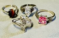 Four sterling silver rings arranged on a textured surface displaying different stones and designs.