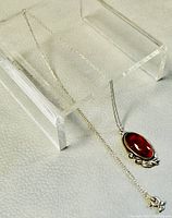 Complete view showing the 21 inch silver chain with the attached amber pendant resting on a textured surface and supported by clear display stands.