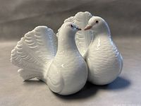 Close-up view of two white porcelain doves with detailed feathers and touching beaks.