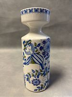 Full view of the candleholder showing hand-painted floral and figure design in blue and green on white ceramic.