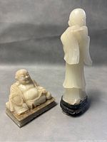 Photo showing the set of two carved stone figurines including the seated Buddha and the standing woman with instrument, highlighting finish and condition.
