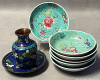 Photo showing the blue cloisonné miniature vase and plate with six hand-painted porcelain plates stacked beside them.