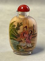 Front view of the glass bottle showing painted scene of two women with greenery and architectural features.