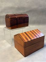 Two handcrafted Sheesham wood boxes: striped two-piece nesting box in front and curved three-piece puzzle box behind on acrylic stand