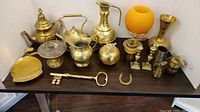 Full lot of assorted brass decor items arranged on a black surface with white background, showing all items together.