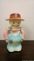 Front view of ceramic cookie jar showing colorful boy figurine with brown hat and blue overalls.