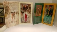 Both Barbie dolls in their original boxes displayed open. Left doll in red and white Victorian-style dress with fur, right doll in green and gold vintage outfit.